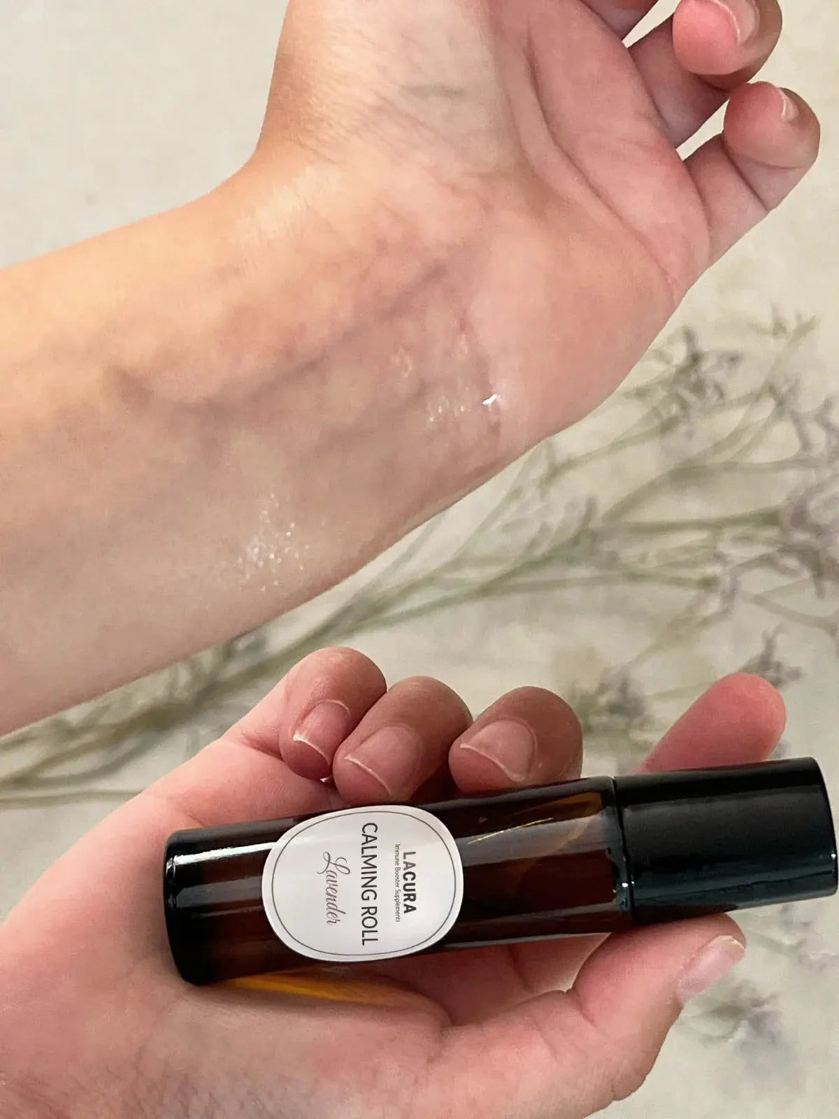 Hand holding a rollerball bottle labeled 'Lacura' with a light background